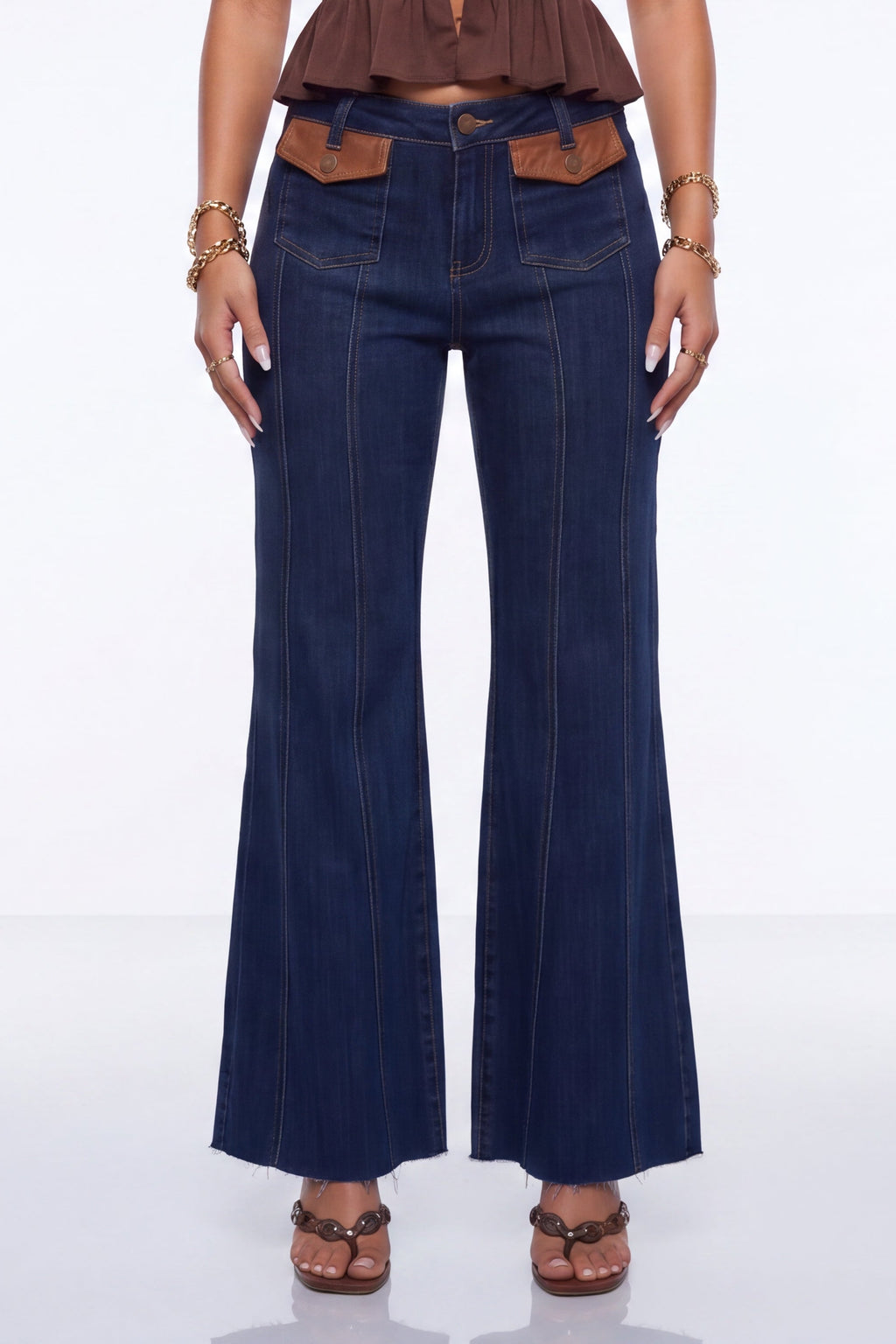 A model wearing dark blue flare jeans with brown leather accents at the waistband and brown sandals, shown from the waist down against a white studio background.