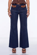 A model wearing dark blue flare jeans with brown leather accents at the waistband and brown sandals, shown from the waist down against a white studio background.
