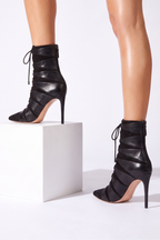 Strappy black vegan leather and matte suede ankle boot with pointed toe and nude stiletto heel, featuring lace-up front and back zip.