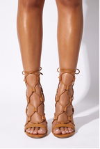 Tan strappy high heel sandals with a round toe and lace-up design, showcasing a sleek, elongated silhouette.